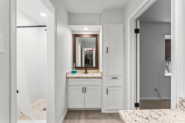 bathroom featuring wood finished floors, vanity, baseboards, a stall shower, and a walk in closet