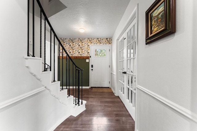 foyer entrance with a textured ceiling, french doors, stairway, dark wood finished floors, and wallpapered walls