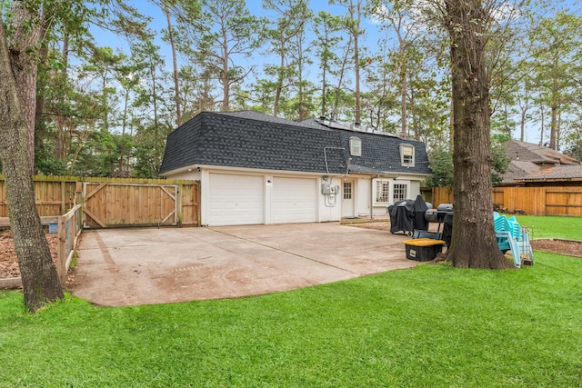 back of house featuring mansard roof, an attached garage, a shingled roof, fence, and a yard