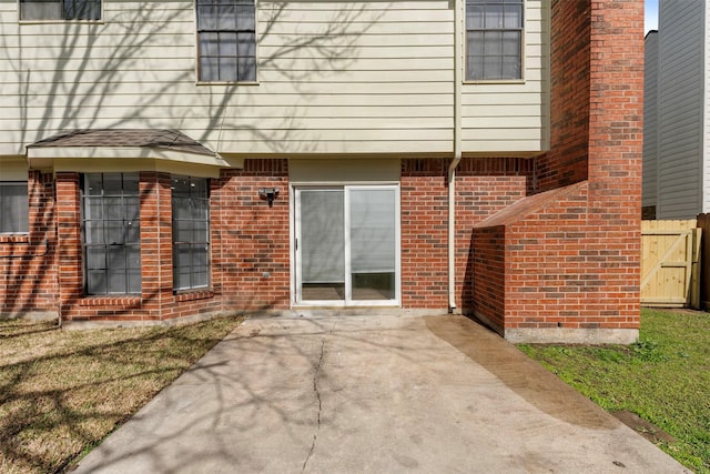 doorway to property featuring a patio area, fence, and brick siding