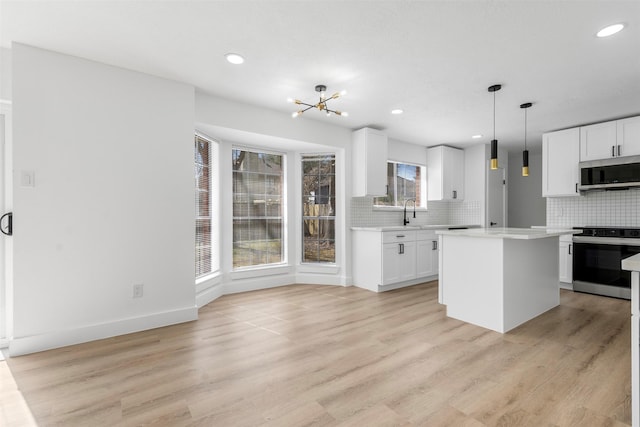 kitchen featuring stainless steel appliances, tasteful backsplash, light countertops, light wood-style flooring, and white cabinetry