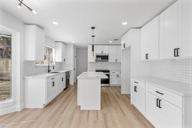 kitchen with stainless steel appliances, light wood finished floors, a sink, and light stone countertops