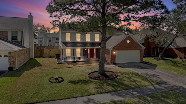 traditional-style home featuring brick siding, covered porch, an attached garage, a front yard, and driveway