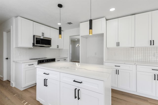 kitchen featuring light stone counters, light wood-style flooring, stainless steel microwave, and visible vents