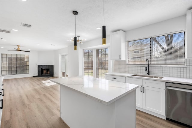 kitchen with tasteful backsplash, visible vents, a kitchen island, stainless steel dishwasher, and a sink