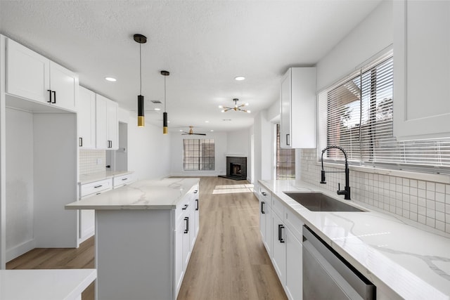 kitchen with dishwasher, open floor plan, a center island, a fireplace, and a sink