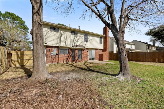 rear view of house with a yard, brick siding, a chimney, and a fenced backyard