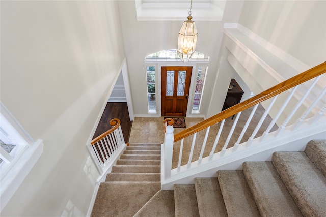 foyer entrance featuring stairway, carpet, a towering ceiling, and an inviting chandelier