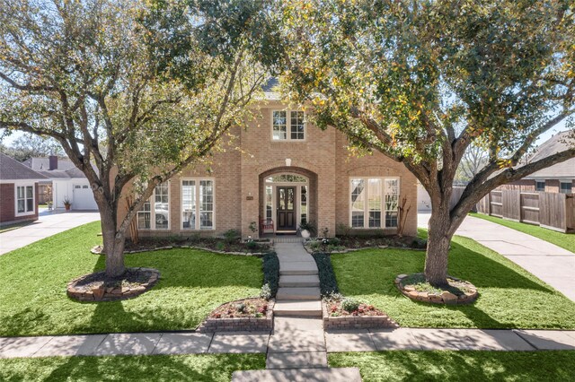 view of front facade with driveway, brick siding, a front yard, and fence