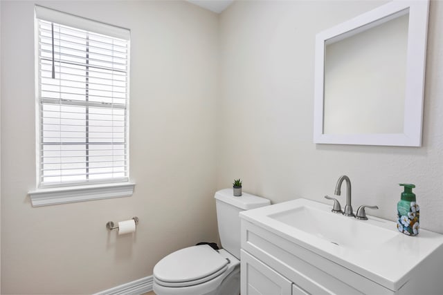 half bathroom featuring toilet, baseboards, and vanity