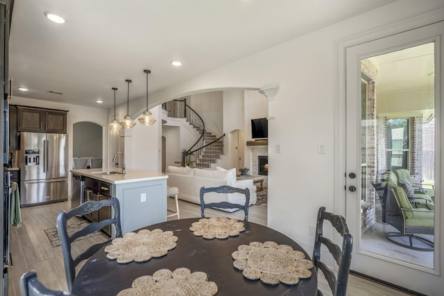 dining area with arched walkways, a fireplace, recessed lighting, light wood-style flooring, and stairs