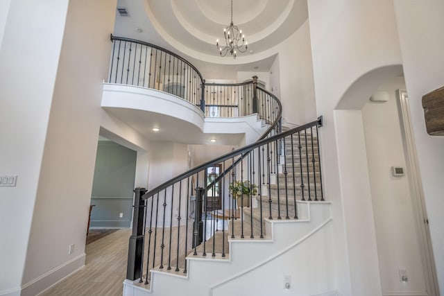 stairway featuring a notable chandelier, visible vents, a towering ceiling, wood finished floors, and baseboards