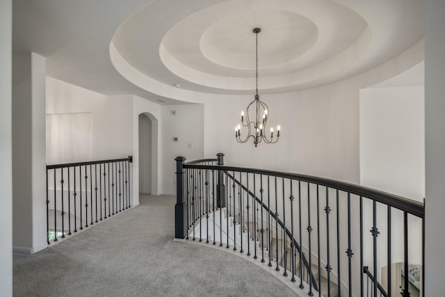 hallway with carpet floors, a tray ceiling, an upstairs landing, and an inviting chandelier