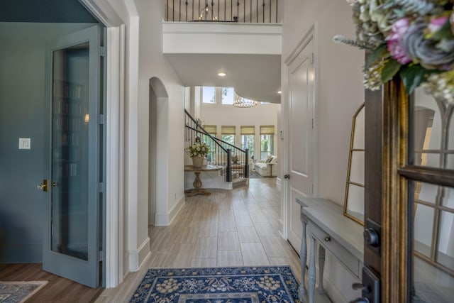 foyer featuring arched walkways, baseboards, stairway, wood tiled floor, and a high ceiling