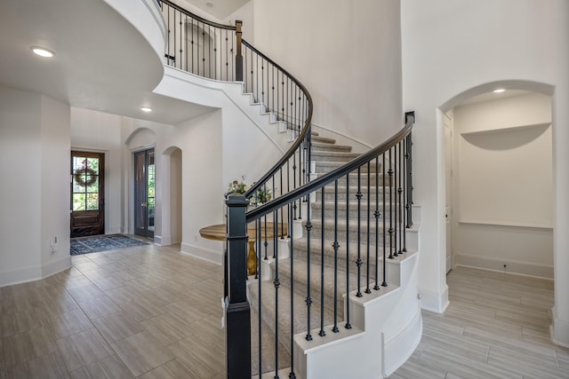 staircase with a towering ceiling, baseboards, arched walkways, and recessed lighting