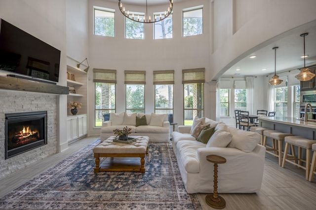 living room with arched walkways, a stone fireplace, wood finished floors, and a notable chandelier