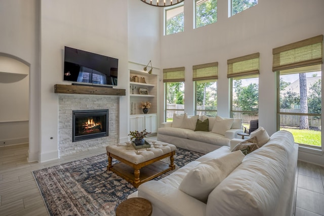 living room with baseboards, built in features, a towering ceiling, wood finished floors, and a fireplace