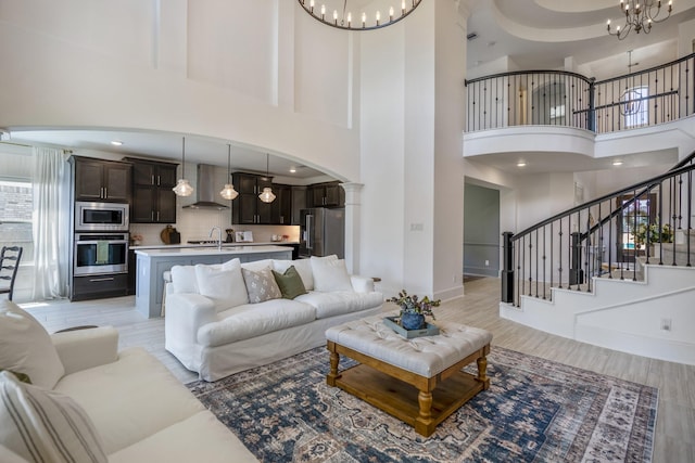 living room featuring light wood finished floors, stairs, a chandelier, and arched walkways