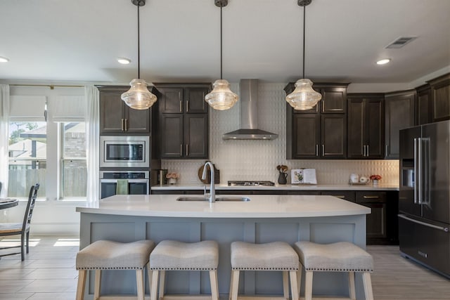 kitchen with stainless steel appliances, decorative backsplash, a sink, wall chimney range hood, and dark brown cabinets