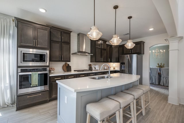 kitchen featuring arched walkways, tasteful backsplash, appliances with stainless steel finishes, a sink, and wall chimney exhaust hood