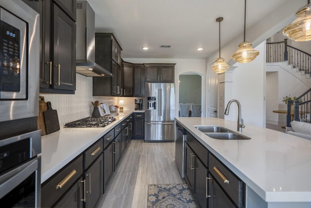 kitchen featuring visible vents, arched walkways, wall chimney exhaust hood, appliances with stainless steel finishes, and a sink