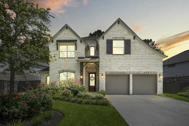 french country inspired facade with driveway, stone siding, an attached garage, and fence