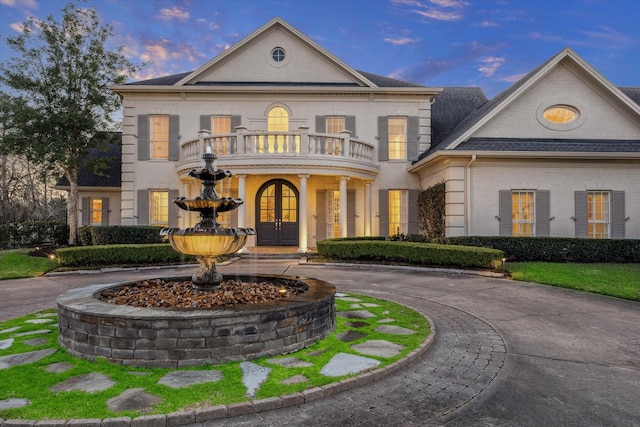 view of front of property with french doors, a balcony, curved driveway, and brick siding