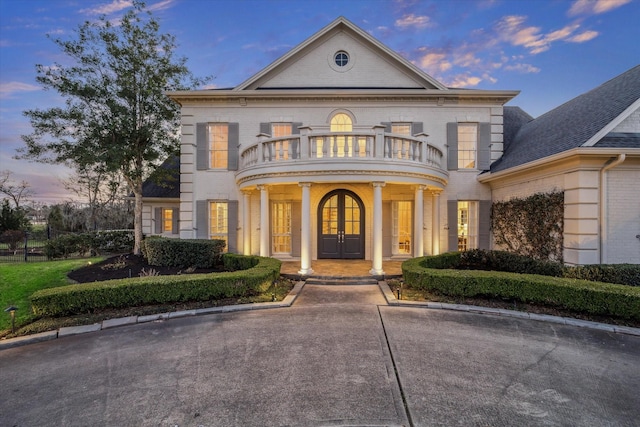 view of front of house featuring brick siding, covered porch, french doors, and a balcony