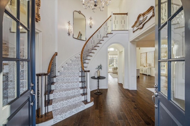 foyer with stairway, a high ceiling, arched walkways, wood-type flooring, and a notable chandelier