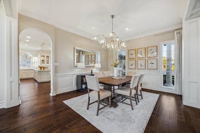 dining space with dark wood finished floors, a decorative wall, arched walkways, and ornamental molding