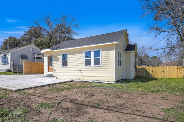 rear view of property with entry steps, fence, and roof with shingles