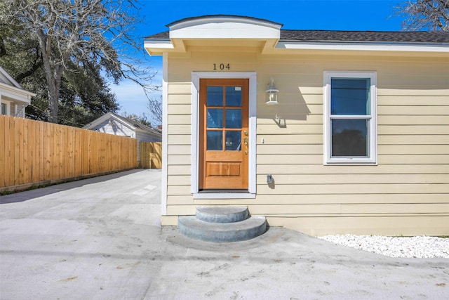 entrance to property featuring roof with shingles, a patio area, and fence