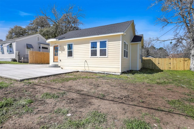 rear view of house with roof with shingles, a patio area, and fence