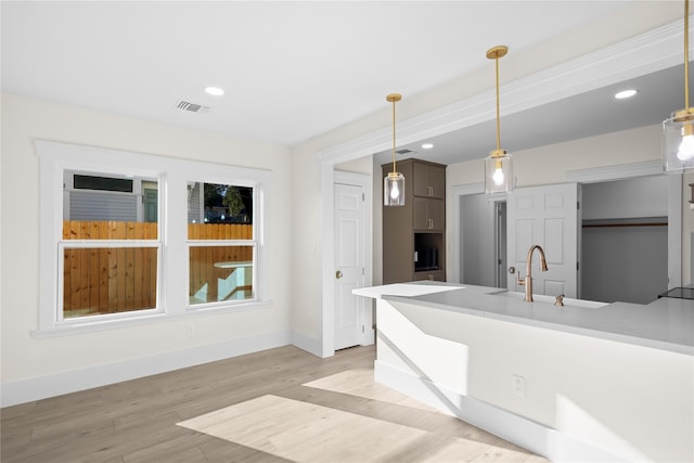 kitchen with light countertops, visible vents, hanging light fixtures, light wood-style flooring, and baseboards