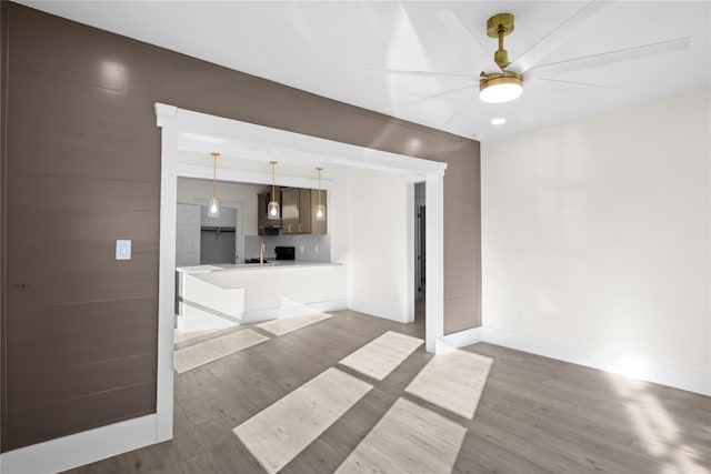 unfurnished living room featuring a sink, ceiling fan, baseboards, and wood finished floors