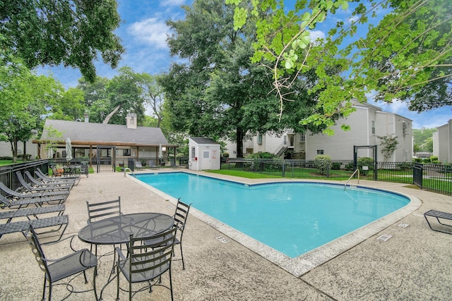 pool with a patio area, a shed, fence, and an outbuilding