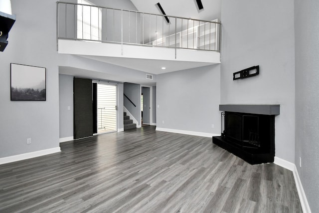 unfurnished living room with a fireplace with raised hearth, wood finished floors, visible vents, baseboards, and stairway