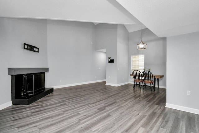 interior space featuring a fireplace with raised hearth, high vaulted ceiling, wood finished floors, and baseboards