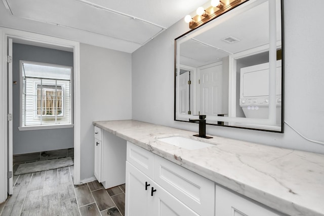 bathroom featuring wood finish floors, stacked washer / dryer, vanity, and baseboards