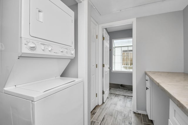 clothes washing area with baseboards, laundry area, stacked washer / dryer, and wood tiled floor