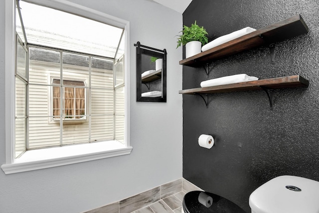 bathroom with a healthy amount of sunlight, baseboards, and toilet