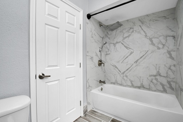 bathroom featuring toilet, shower / bathing tub combination, and a textured wall