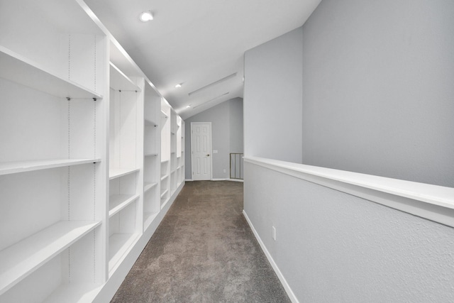 hallway with lofted ceiling, baseboards, and dark carpet