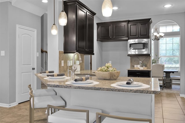 kitchen featuring a peninsula, a sink, decorative backsplash, stainless steel microwave, and a kitchen bar