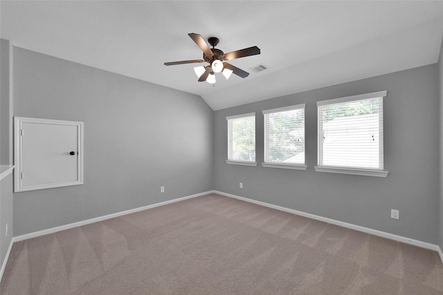 carpeted empty room featuring a ceiling fan, visible vents, vaulted ceiling, and baseboards