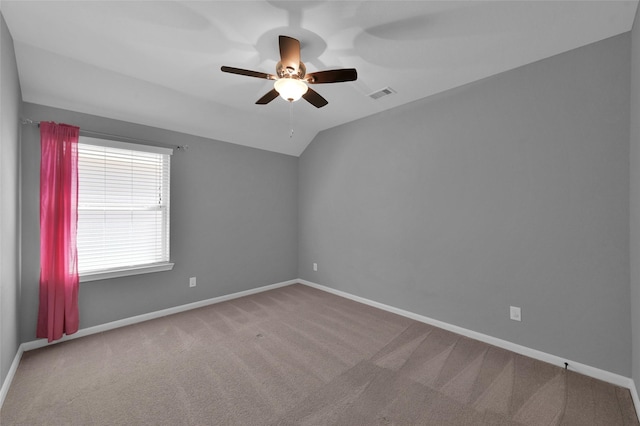 carpeted empty room with vaulted ceiling, a ceiling fan, visible vents, and baseboards