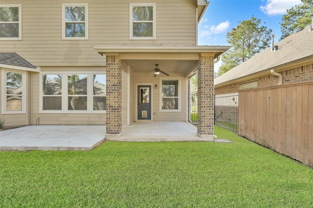 doorway to property featuring a ceiling fan, a lawn, a patio, fence, and brick siding