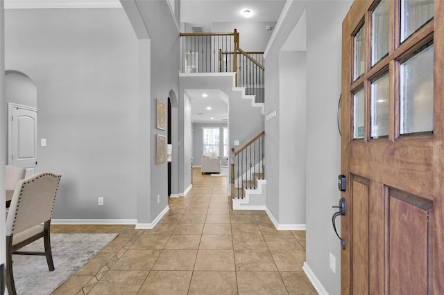 foyer featuring arched walkways, light tile patterned floors, a high ceiling, baseboards, and stairs