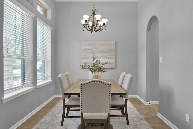 dining room with tile patterned flooring, arched walkways, a chandelier, and baseboards