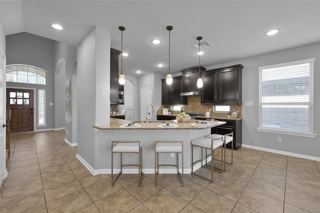 kitchen featuring arched walkways, plenty of natural light, under cabinet range hood, and decorative backsplash